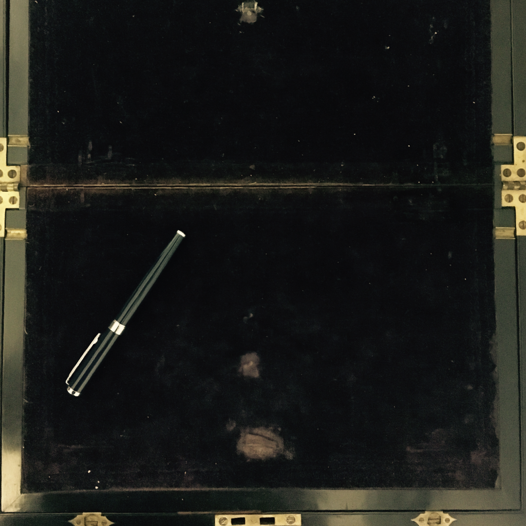 The interior of an antique writing slope, showing a dark purple velvet surface for writing on.